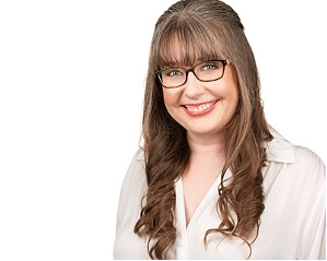 Smiling woman with long, wavy brown hair and bangs, wearing glasses and a white blouse, poses against a plain white background.